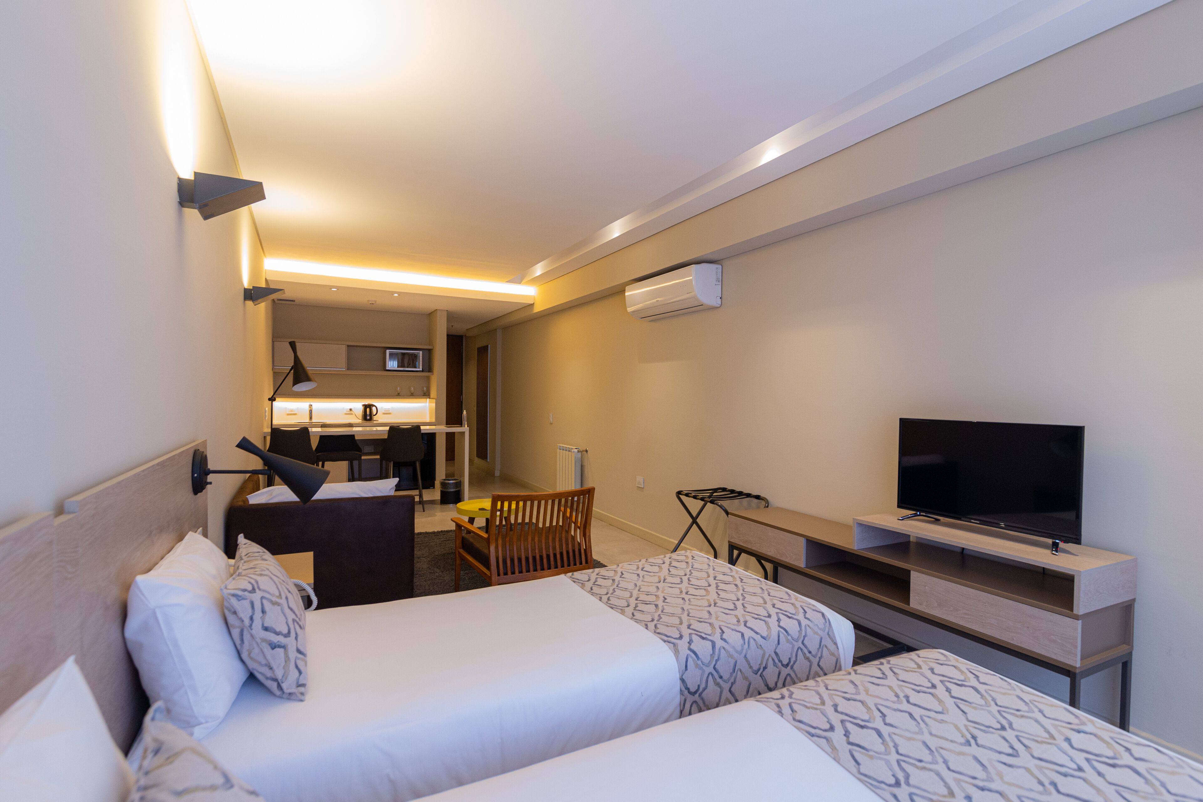 A hotel room with two beds, a desk, a chair, a television, and an air conditioning unit.