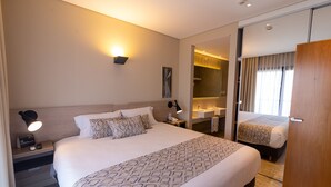 Une chambre d’hôtel avec un grand lit, des tables de chevet, un miroir, une armoire et une salle de bain équipée d’un lavabo et d’un miroir.