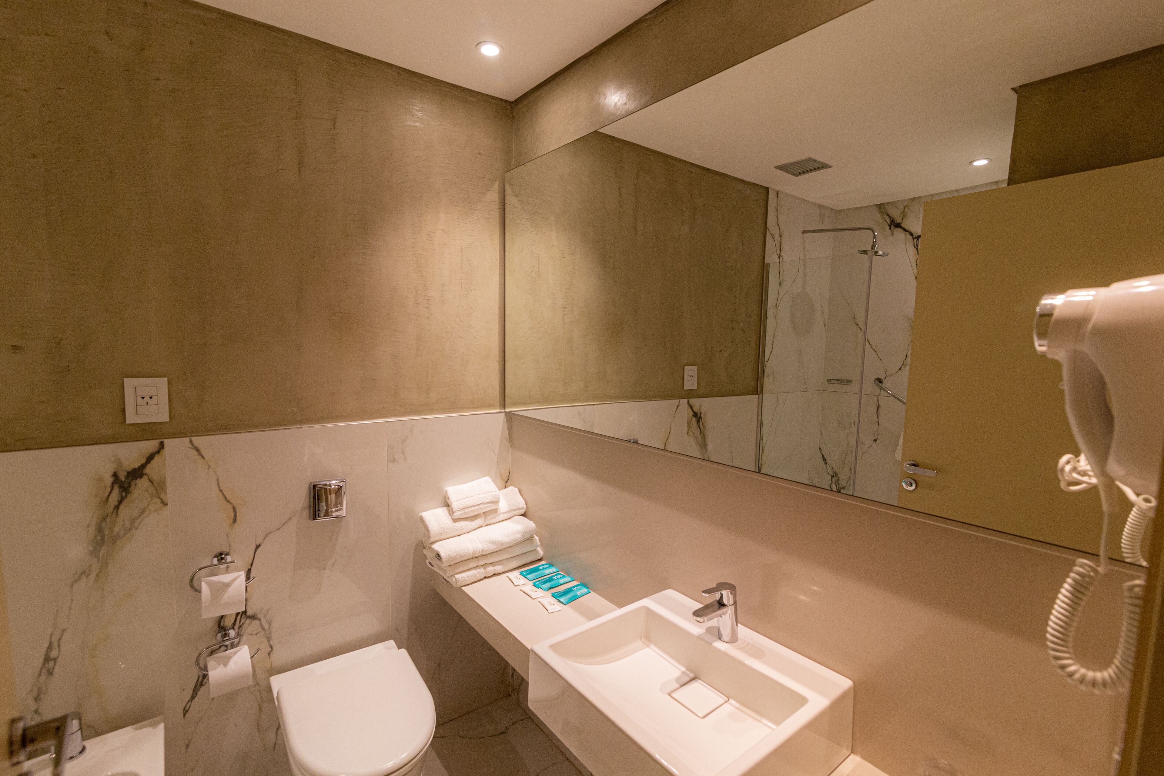 A modern bathroom with a marble wall, a white sink, a toilet, and a hairdryer.