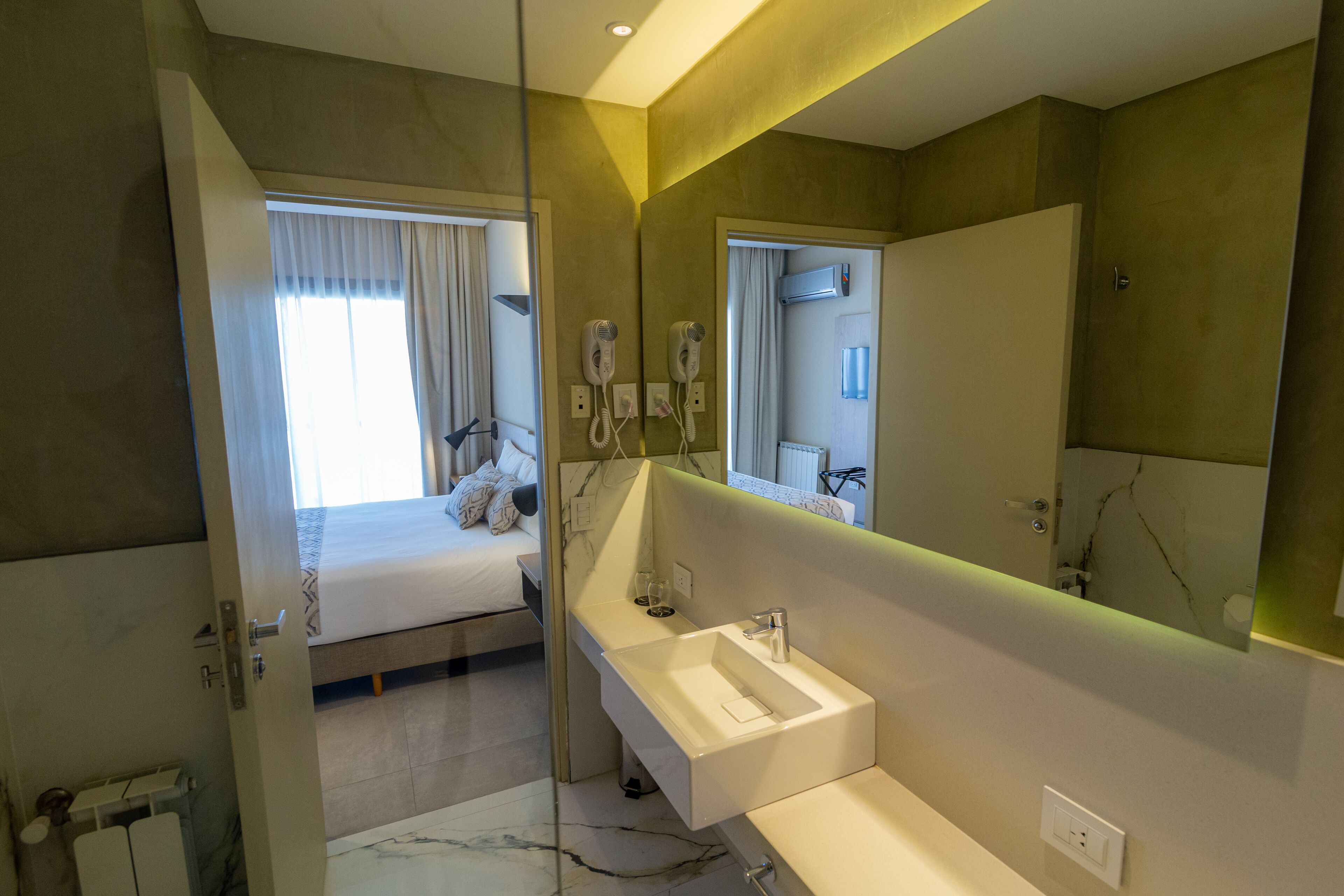 A modern hotel bathroom with a large mirror, a built-in sink, and a hairdryer.