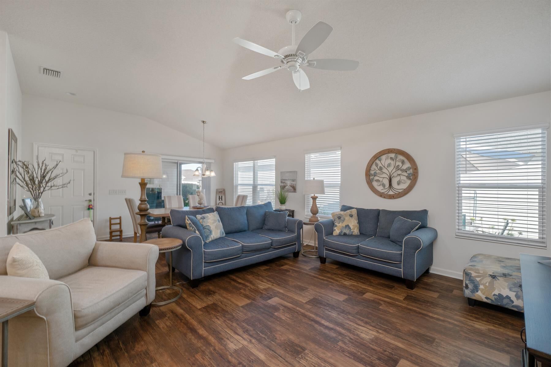 A spacious living room with two blue sofas, a white armchair, and a wooden floor.