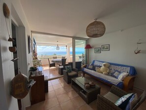 Una sala de estar con sofá, mesa de centro y vista a la playa.