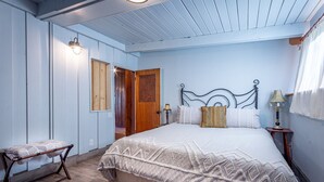 Een slaapkamer met een bed, een bankje en een deur die naar een andere kamer leidt.