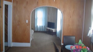 A living room with a ceiling fan, wooden walls, a TV, and a floral arrangement. - The Little Sunflower (Jetmore)