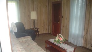 A living room with a sofa, a table with a floral tablecloth, a lamp, and a chair. - The Little Sunflower (Jetmore)