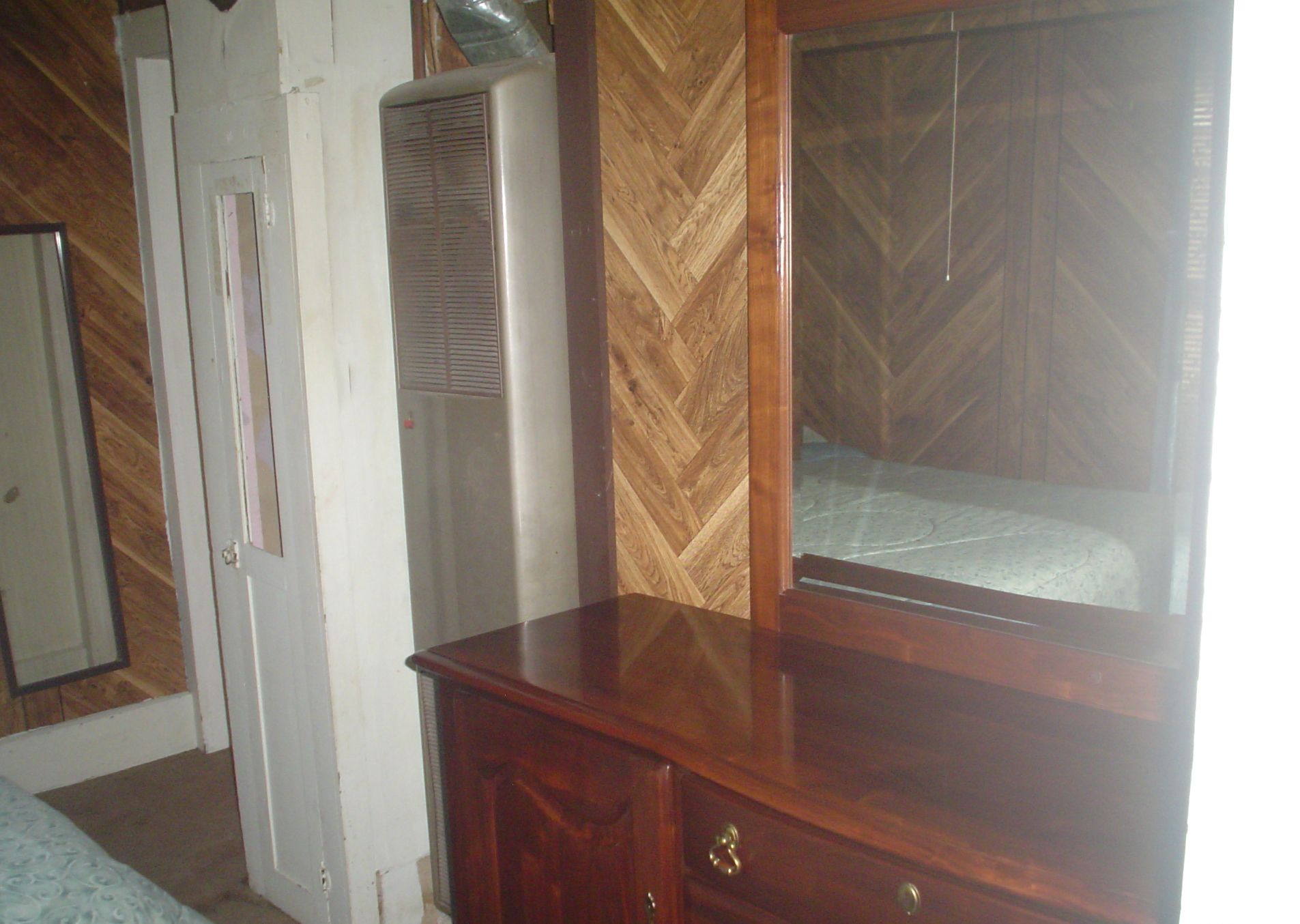 A room with a wooden dresser, a mirror, and a vent.
