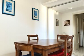 A dining area with a wooden table and chairs, framed pictures on the walls, and a door leading to another room.