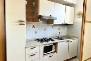 Kompakti keittiö, jossa on kaasuliesi, mikroaaltouuni, pesuallas ja valkoiset kaapit.
