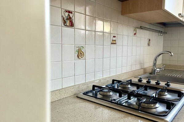 A kitchen with a gas stove, a sink, and decorative tiles on the wall.