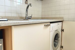 A kitchen with a stainless steel sink, a built-in washing machine, and a tiled backsplash.