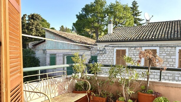 A balcony with a metal chair, potted plants, and a view of a stone building with a tiled roof. - S256 - Sirolo, comfortable apartment in the center (Sirolo)