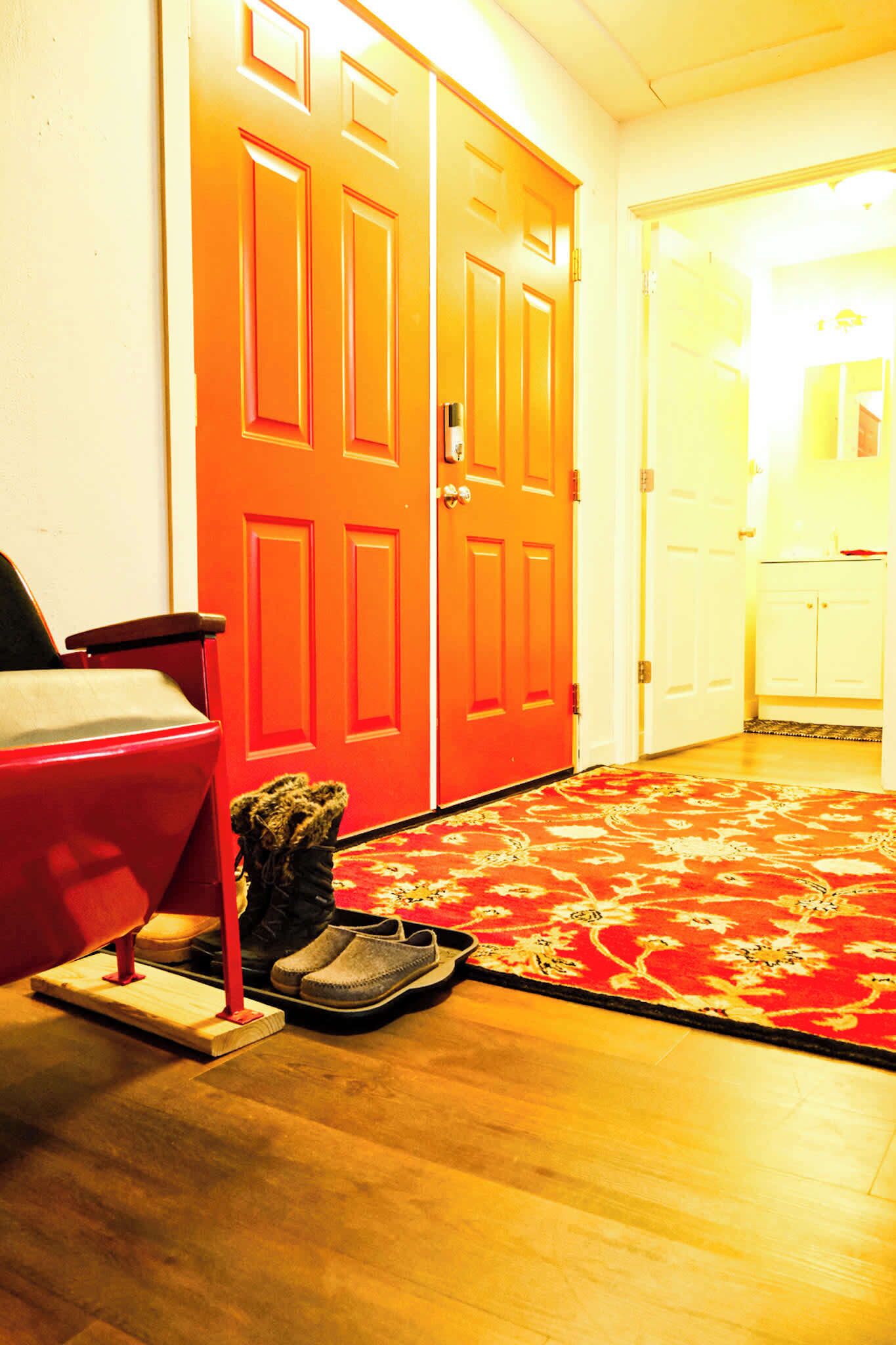 Una habitación con puerta roja, suelo de madera y alfombra roja.