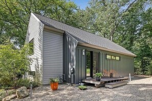 Une maison moderne avec un toit en pente, un porche à l’avant doté de sièges et une allée gravillonnée.
