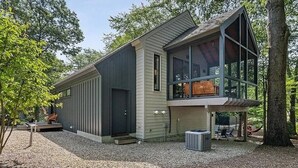 A modern house with a large glass window, a covered porch, and a gravel driveway.