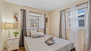 Een slaapkamer met een bed, nachtkastje, lamp en gordijnen.