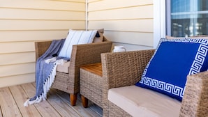 Een rieten bank met een blauw kussen en een gestreept plaid op een houten terras.