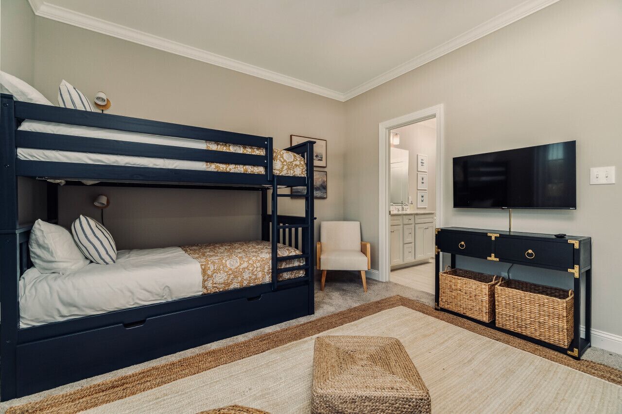 A room with a bunk bed, a chair, a TV, and a console table with baskets.