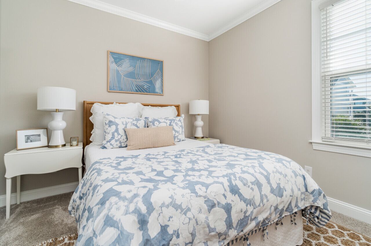 A bedroom with a bed, two bedside tables, a nightstand, a framed picture, and a window with blinds.