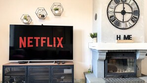 A living room with a TV displaying the Netflix logo, a fireplace, and three hexagonal wall decorations. - Carcalove - Pool, Billard & Jacuzzi - 10pax (Fontiès-d'Aude)