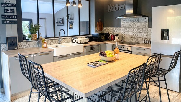A modern kitchen with a large island, black chairs, and a variety of appliances. - Carcalove - Pool, Billard & Jacuzzi - 10pax (Fontiès-d'Aude)