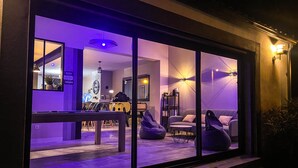 A modern interior with a large window, a sofa, a coffee table, and a bookshelf. - Carcalove - Pool, Billard & Jacuzzi - 10pax (Fontiès-d'Aude)