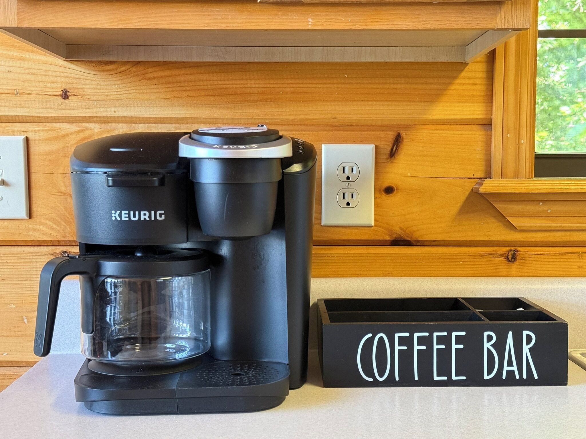 A Keurig coffee maker on a countertop with a coffee bar sign.