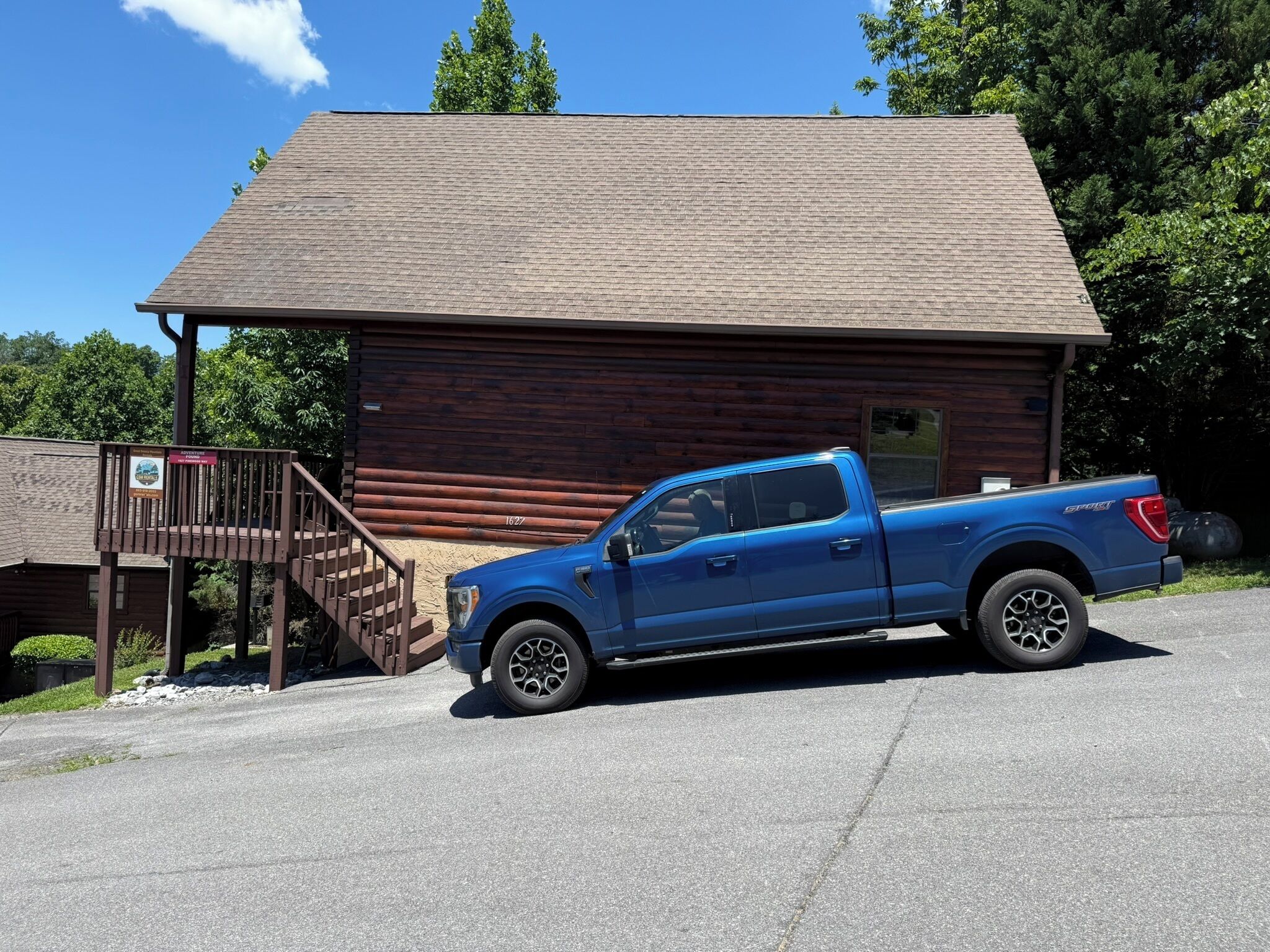 Ein blauer Pickup vor einer Holzhütte mit einer Treppe, die zu einer Terrasse führt.