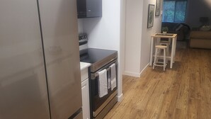 Una cocina moderna con electrodomésticos de acero inoxidable, piso de madera y un pequeño comedor con taburetes.