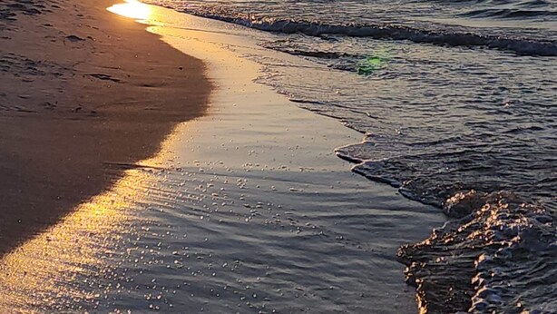 Una playa al atardecer, con el sol bajo en el horizonte, reflejándose en el agua.