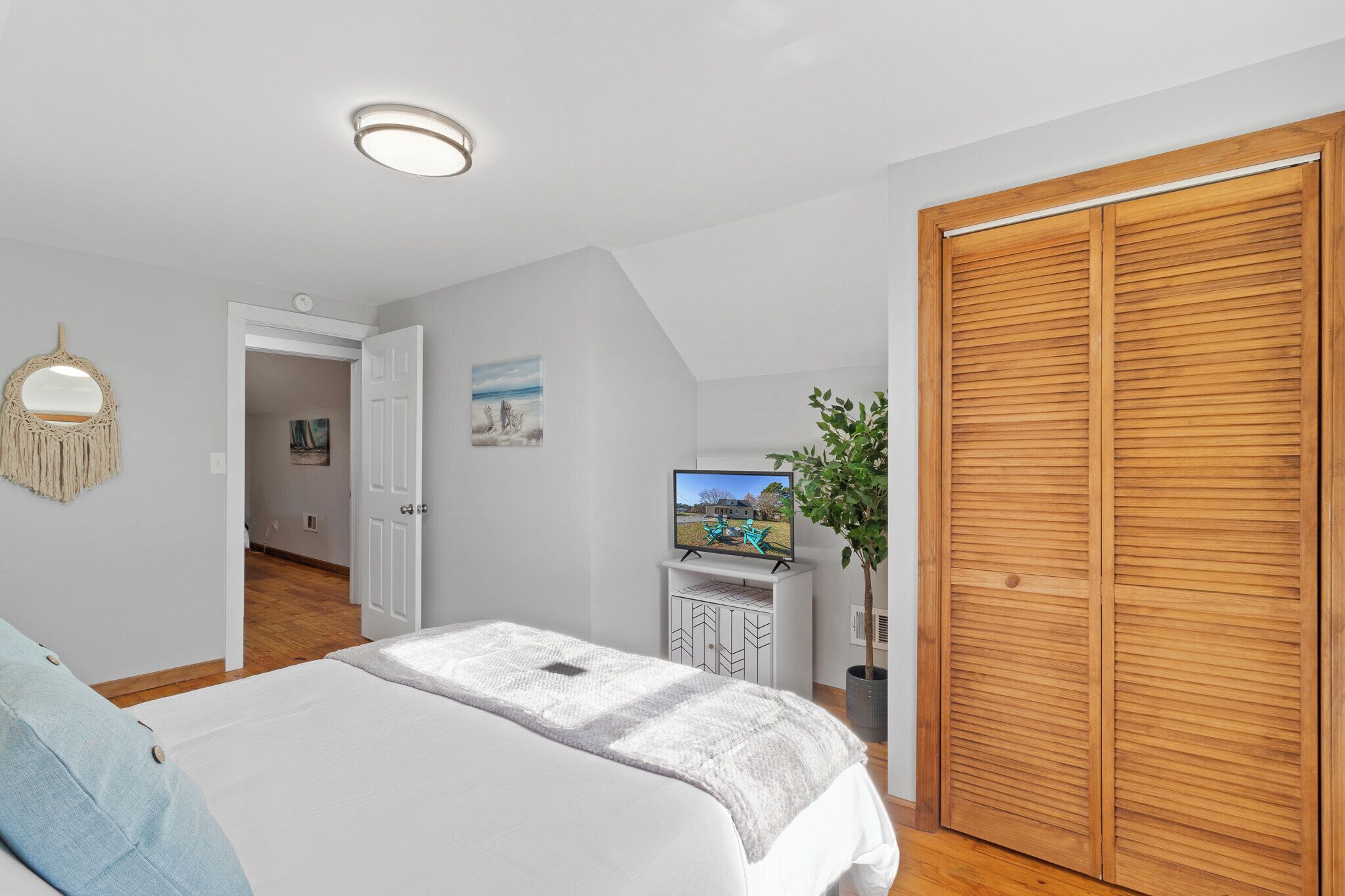 A bedroom with a bed, a wooden wardrobe, a television on a stand, and a door leading to another room.