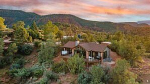Una casa moderna con una amplia terraza, rodeada de vegetación densa y colinas al fondo.