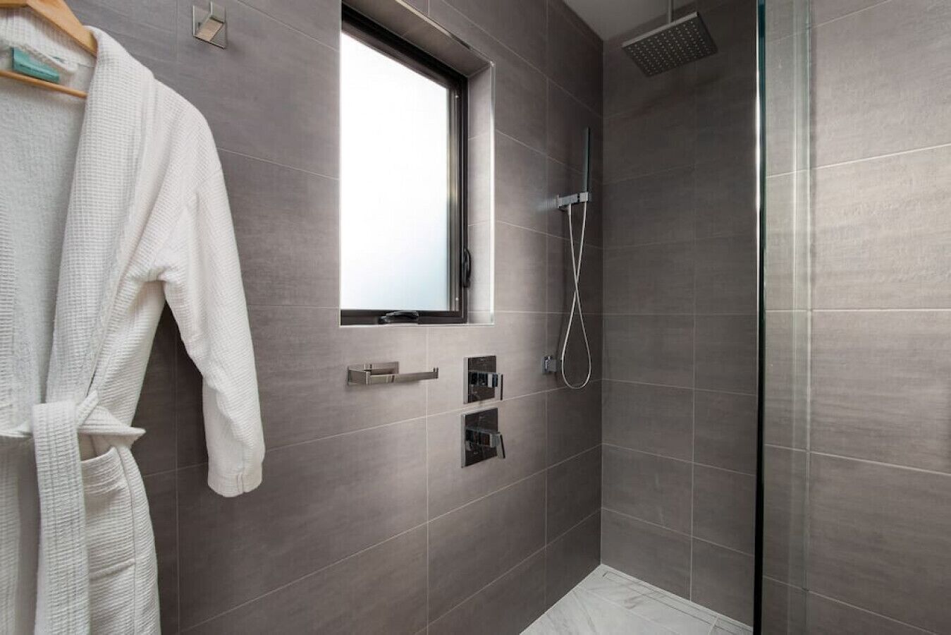 Ein modernes Badezimmer mit begehbarer Dusche, einem Fenster und einem Handtuchhalter.