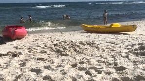 En sandstrand med to kajakker, en lyserød og en gul, og mennesker i vandet.