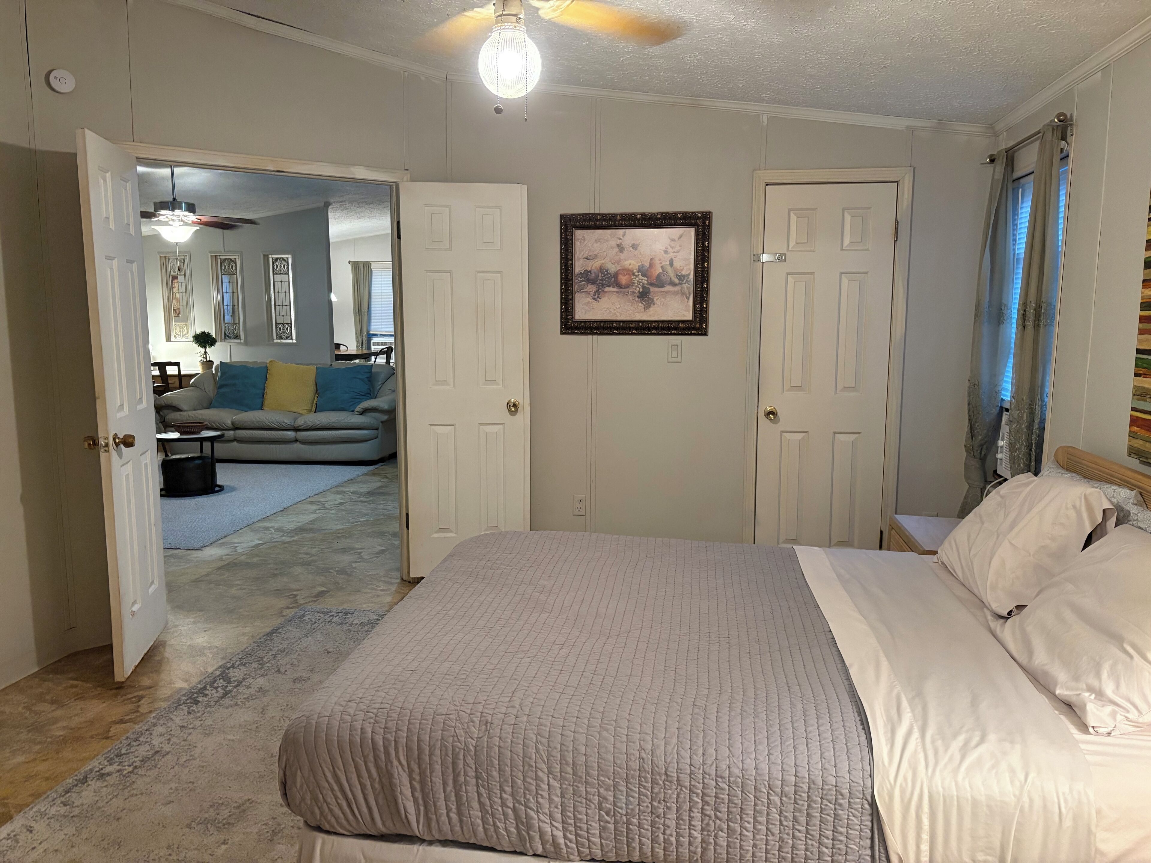 Une chambre à coucher avec un lit, une porte donnant sur le salon et un ventilateur de plafond.
