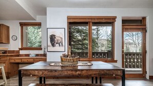 A rustic kitchen with wooden cabinets, a large wooden table, and a framed picture of a bison on the wall. - Luxurious Condo Gated Community Pool Hot Tubs (Edwards)