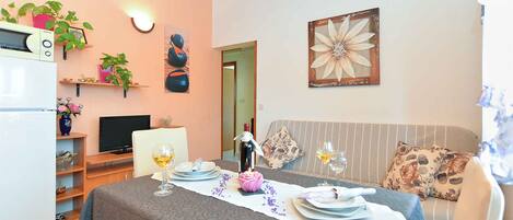 A dining area with a table set for two, a television, and a sofa with floral cushions.