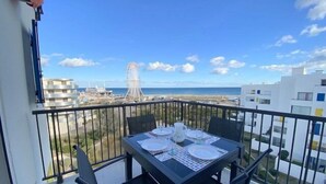Un balcon avec une table dressée pour deux personnes, donnant sur une plage et une grande roue.