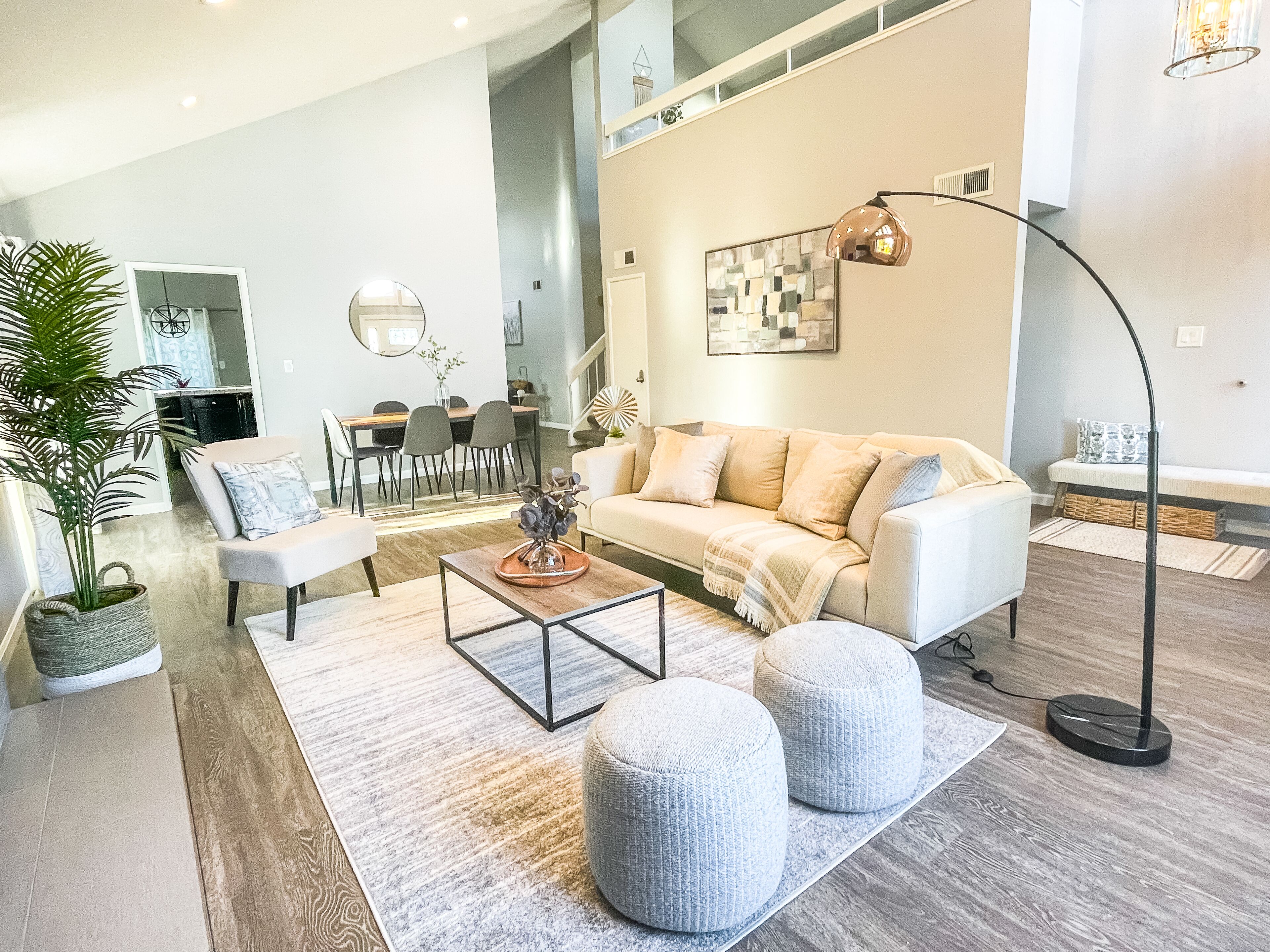 Un salon moderne avec un canapé, des poufs, une table basse et, au fond, un coin repas.