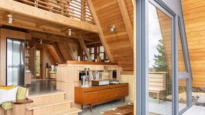 Een modern ingericht blokhutinterieur met een houten trap, een eethoek en een grote glazen deur naar buiten.