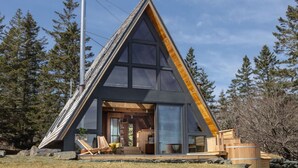 Een modern A-frame vakantiehuis met grote ramen, een houten terras en vrij uitzicht op het omliggende bos.