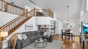 A spacious living area with a gray sectional sofa, a coffee table, and a dining table with chairs. A wooden staircase leads to an upper level. - HOT TUB | Lake Front | Lavender Home (Burt)