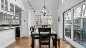 A modern kitchen with white cabinets, a dining area with a wooden table and chairs, and large windows providing views of the outdoors. - HOT TUB | Lake Front | Lavender Home (Burt)