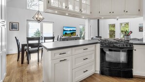 A modern kitchen with white cabinetry, a central island with a stove, and a dining area with a chandelier. - HOT TUB | Lake Front | Lavender Home (Burt)
