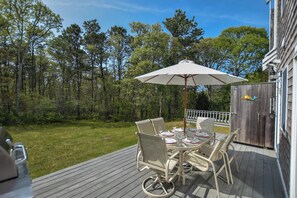 An outdoor deck with a table and chairs, surrounded by a wooden deck and a grassy lawn.