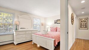 A bedroom with a white dresser, a bed with a red and white checkered bedspread, and a window with blinds.
