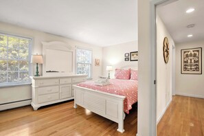 A bedroom with a white dresser, a bed with a red and white checkered bedspread, and a window with blinds.