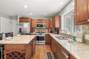 A kitchen with wooden cabinets, stainless steel appliances, a large window, and a marble countertop.