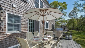An outdoor dining area with a table and chairs, a grill, and a large umbrella. - Close to Bike Path 1 Mile to Beaches! (South Chatham)