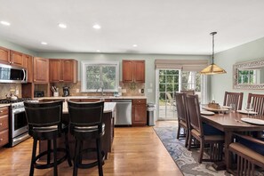 A kitchen with wooden cabinets, a stainless steel range, and a dining area with a table and chairs.
