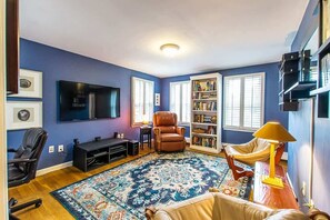 Ein Wohnzimmer mit Flachbildfernseher, Ledersesseln, Bücherregal und einem gemusterten Teppich.